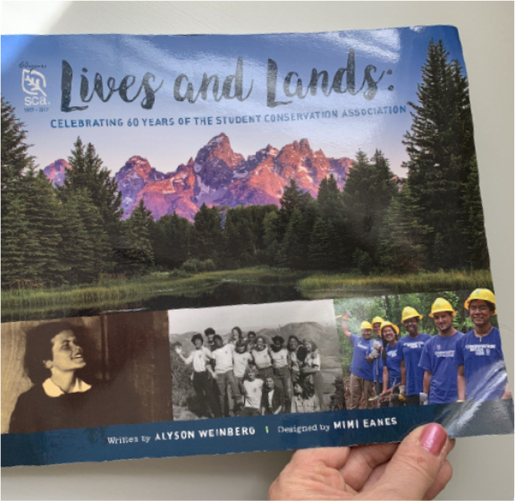 lives and lands book cover with book held by mimi's hand at bottom, about to open it